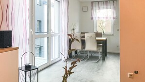 A modern living room with large windows, a dining area, and a TV on a stand. - Cozy apartment in Rechlin with lake view (Rechlin)