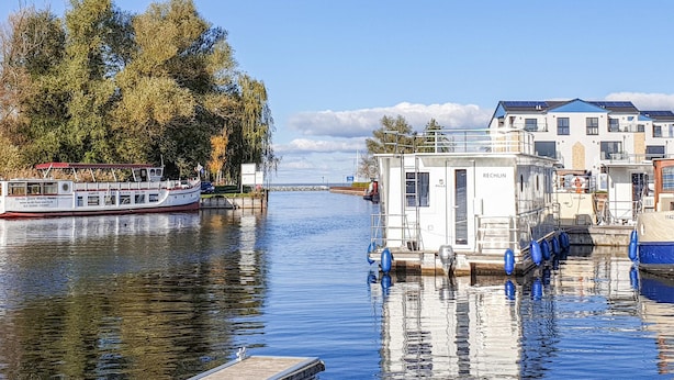 A calm river with a docked boat and a small houseboat named RECHLIN. - Cozy apartment in Rechlin with lake view (Rechlin)