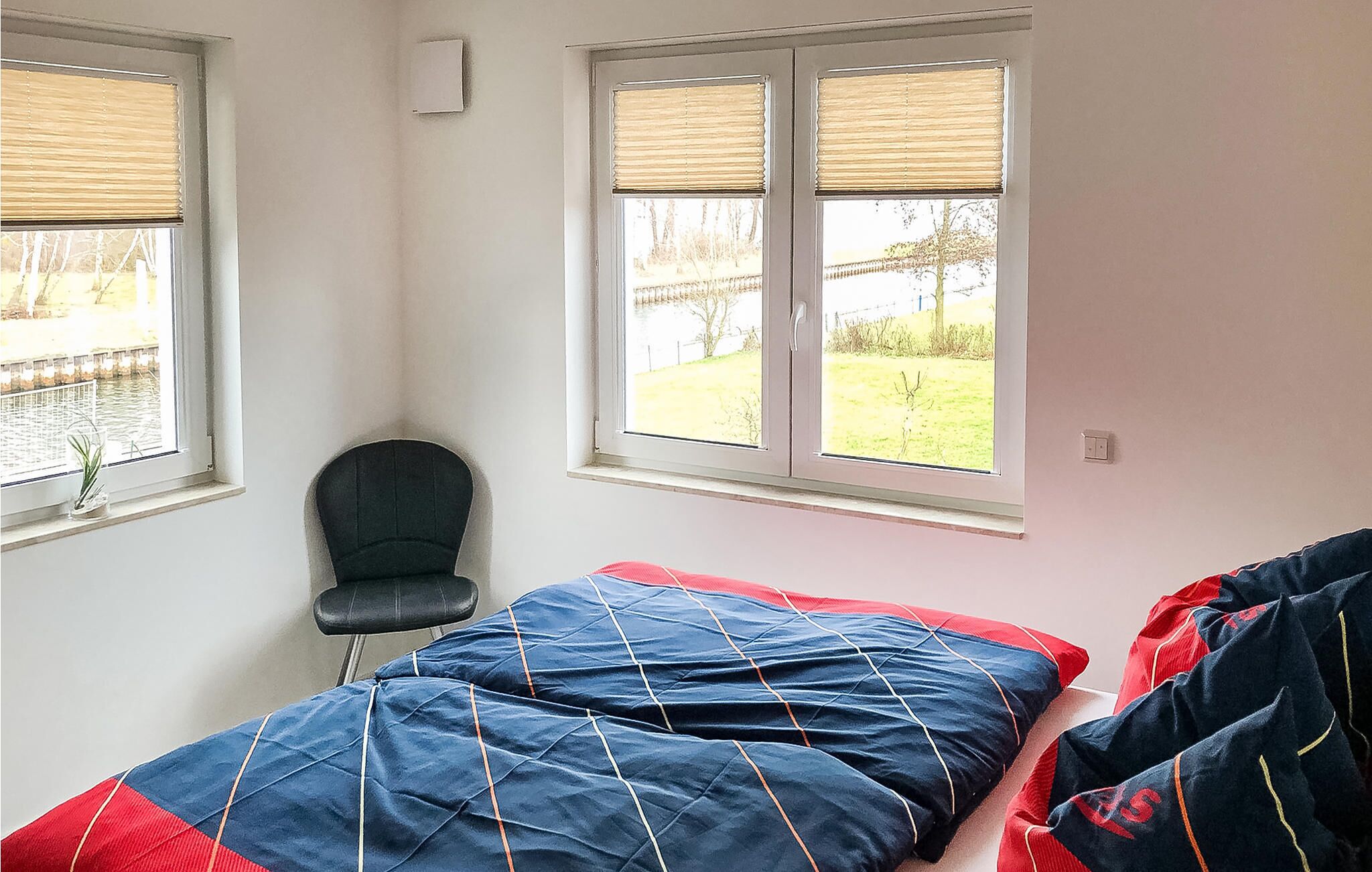 A bedroom with a bed, a chair, and two windows with blinds.