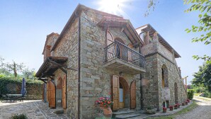 A stone building with a balcony, wooden doors, and potted plants. - La Casella- La Terrazza (Castelfranco di Sopra)