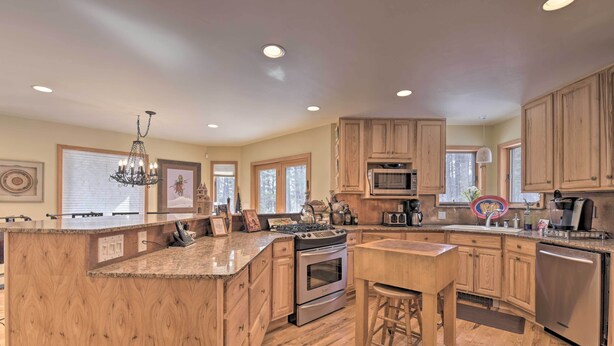 A spacious kitchen with wooden cabinets, a granite countertop, stainless steel appliances, and a chandelier. - Spacious Angel Fire Cabin < 4 Miles to Resort! (Angel Fire)