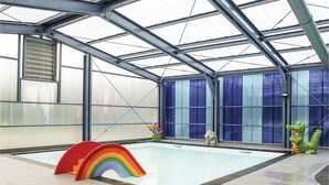 Een binnenzwembad met een glazen dak, een constructie in de vorm van een regenboog en dierenbeeldjes uit een tekenfilm.
