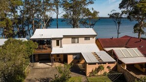 Ein zweistöckiges Haus mit einer großen Terrasse und einer Garage, umgeben von Bäumen und einem Gewässer.