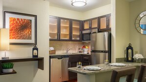 Una cocina moderna con armarios oscuros, electrodomésticos de acero inoxidable y una pequeña zona de comedor con mesa y sillas.