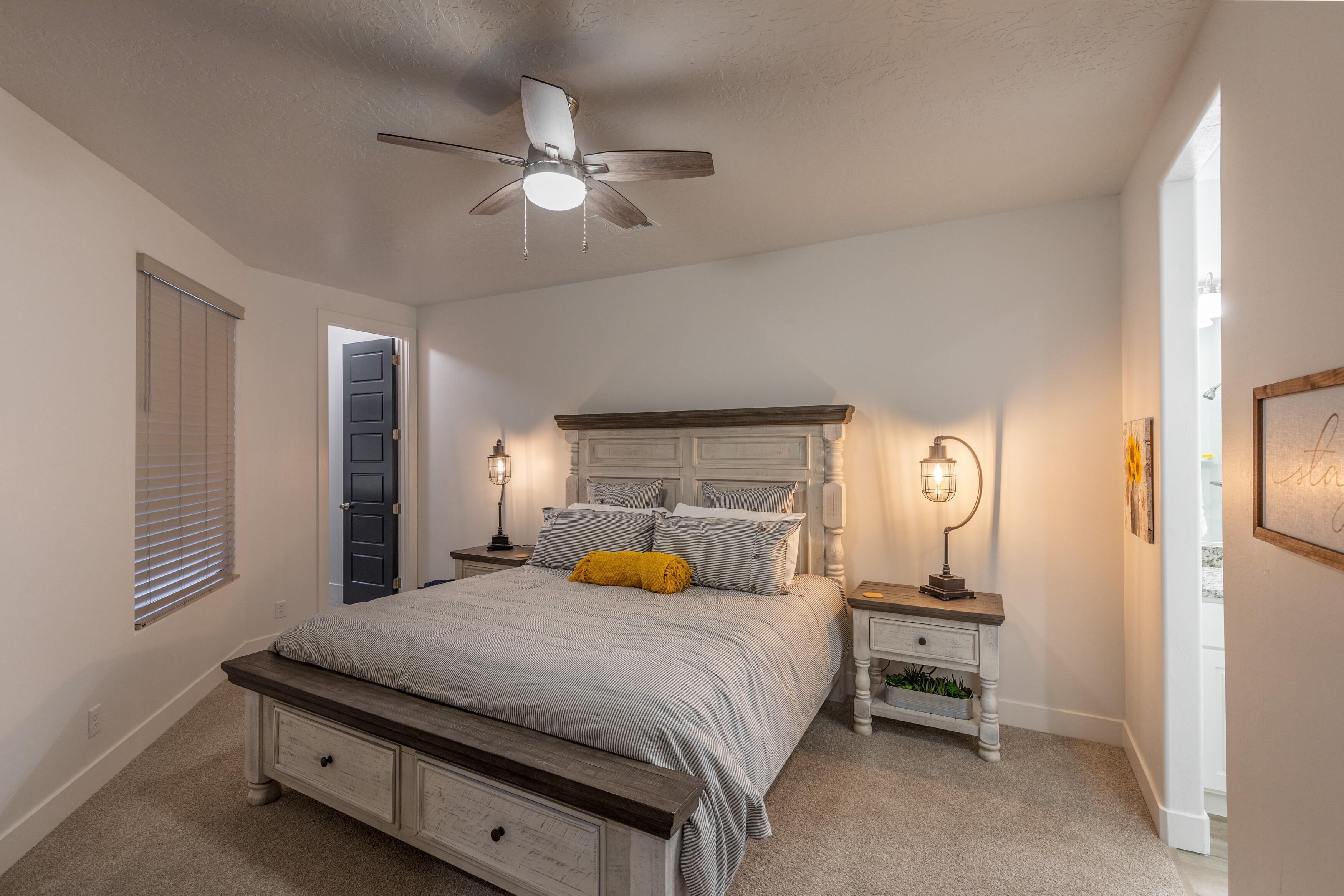 A bedroom with a bed, bedside tables, a ceiling fan, and a window with blinds.