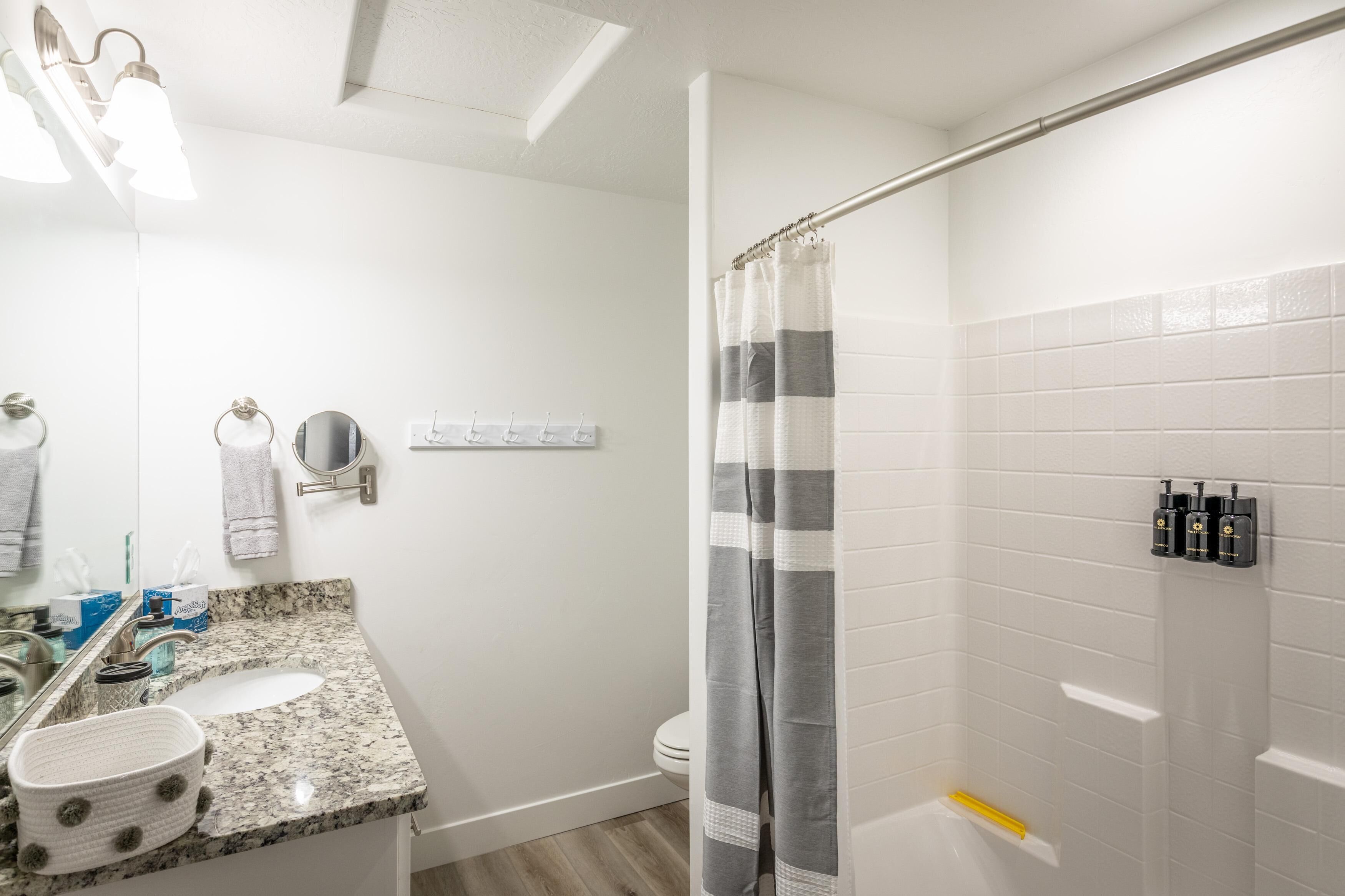 A bathroom with a granite countertop sink, a mirror, a towel rack, a toilet, and a shower with a striped curtain.