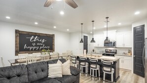 Una cocina moderna con armarios blancos, un refrigerador negro y una zona de comedor con un sofá negro y sillas blancas.