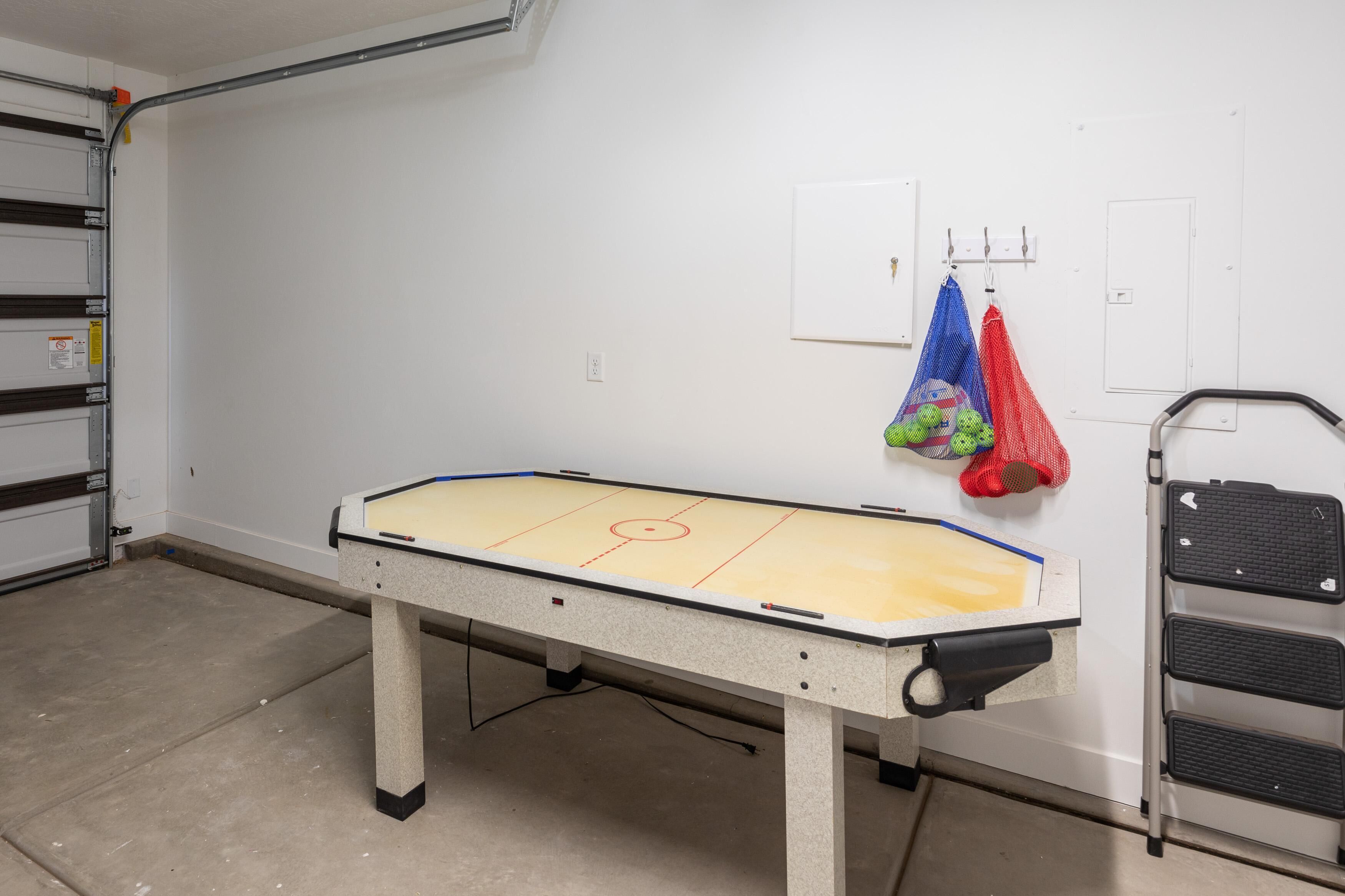 Una mesa de ping pong en una habitación con paredes blancas, una escalera metálica y dos bolsas colgadas de ganchos.