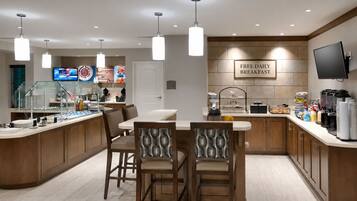 A modern kitchen with a breakfast bar, a TV, and a sign offering free daily breakfast.