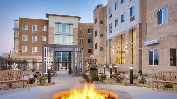 A courtyard with a fire pit, benches, and a building with multiple floors and large windows.