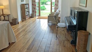 Une pièce chaleureuse avec un plancher en bois, un piano, des meubles en osier et une bibliothèque.