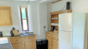 Une cuisine avec des meubles en bois, un réfrigérateur blanc, une fenêtre avec des stores et un plan de travail sur lequel se trouvent divers objets.
