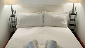 Un lit bien fait, avec du linge de lit blanc, deux lampes de chevet et des serviettes pliées posées sur le lit.