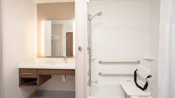 A modern bathroom with a white sink, mirror, and shower. It includes a grab bar for safety and a towel rack.