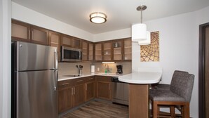 A modern kitchen with stainless steel appliances, wooden cabinets, and a bar area with a chair.