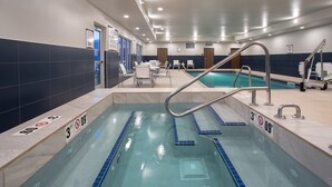A swimming pool with clear lane markings, a diving board, and a lounge area with chairs and tables.