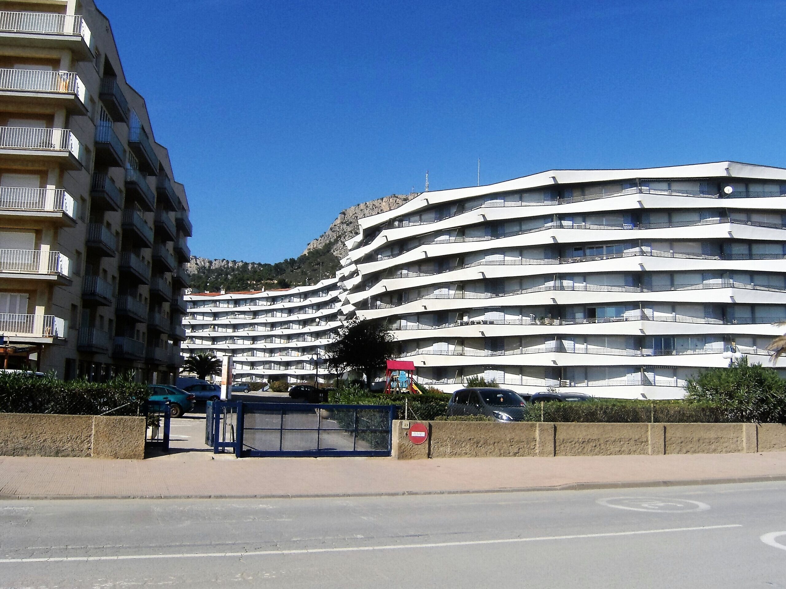 Un hôtel à plusieurs étages, doté de balcons, d’un parking et surplombant un ciel d’un bleu limpide.