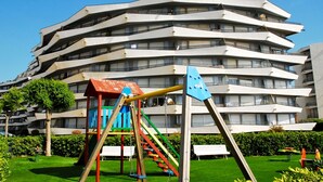 A playground with swings and a climbing structure in front of a multi-story building. - ROCAMAURA II 1-5 (Estartit)