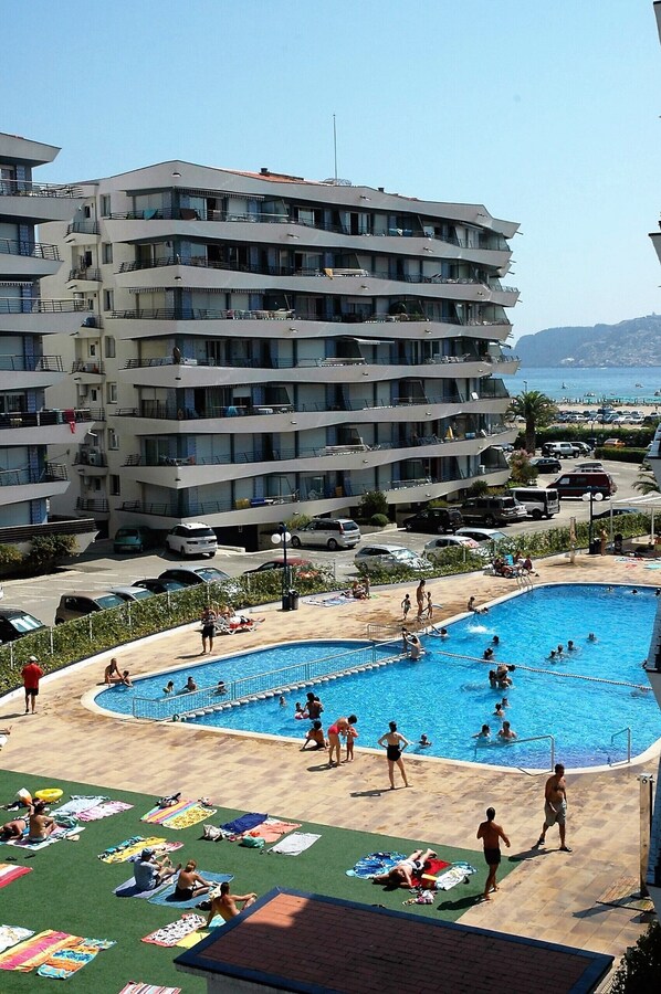 A multi-story hotel with a swimming pool, outdoor seating, and a view of the sea.