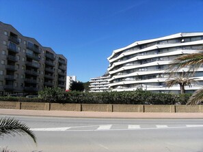 A multi-story building with balconies, a clear sky, and a palm tree in the foreground.