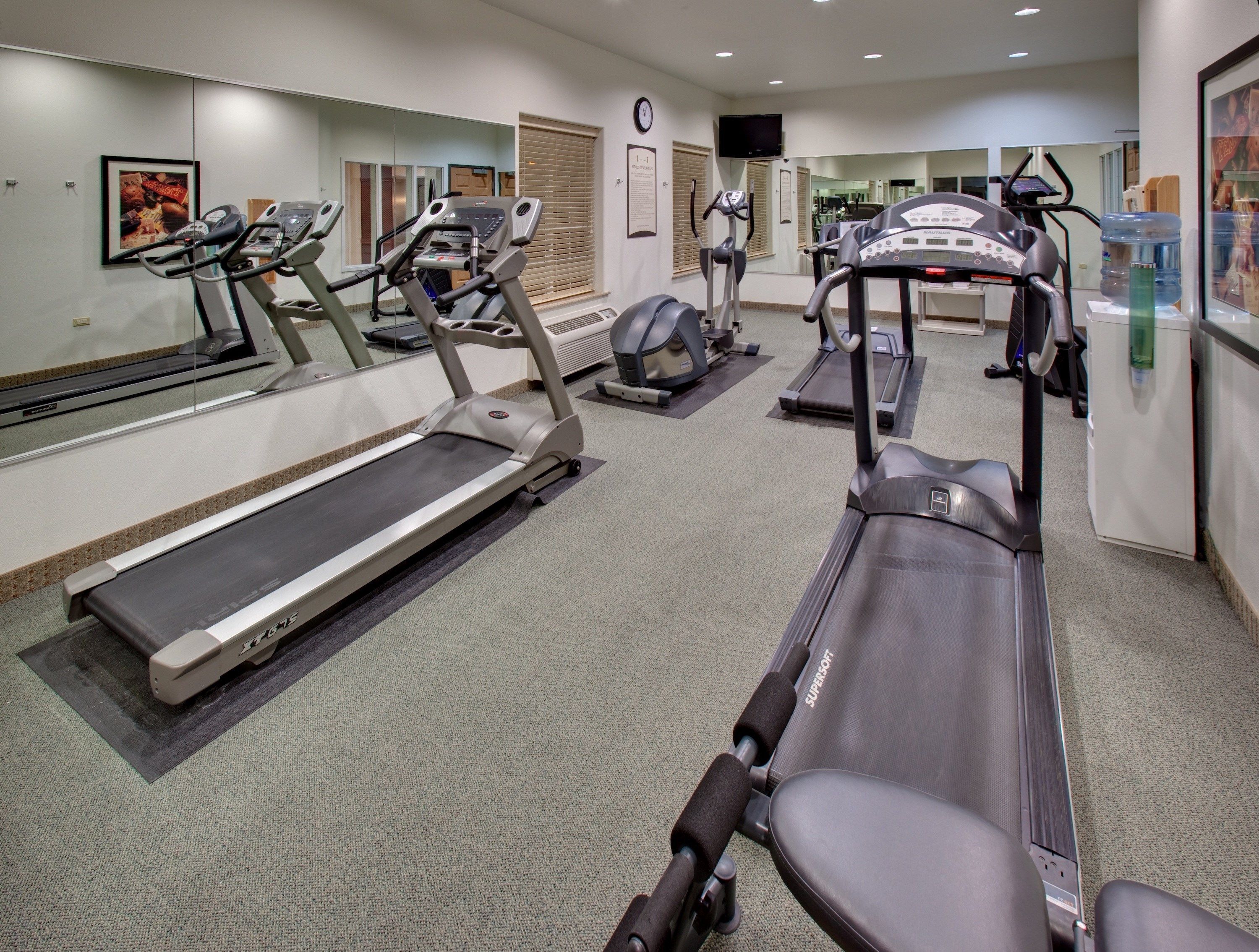 Une salle de sport équipée de tapis de course, de vélos elliptiques et d’un distributeur d’eau.
