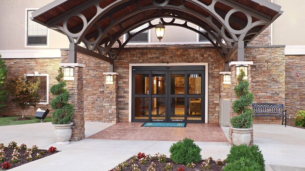A hotel entrance with a stone facade, a wooden archway, and a blue mat with "TRAVELER'S" written on it.