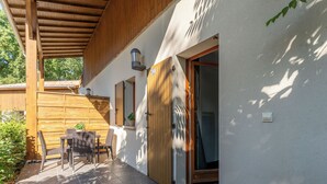 A covered patio with a table and chairs, a wooden door, and a window. - Appart charmant + accès piscine (Lacanau)