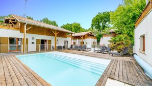 Un espace piscine doté d’une terrasse en bois, de chaises longues et d’un coin salon abrité.