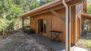 A wooden cabin with a patio, a door, and a table with benches.