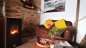 A cozy living room with a fireplace, a sofa with yellow cushions, a vase with flowers, and a painting of a coastal scene. - 5routes apartments connecting with nature (Vimianzo)