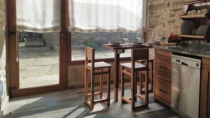 A kitchen with a stone wall, wooden chairs, a table, and a dishwasher. - 5routes apartments connecting with nature (Vimianzo)