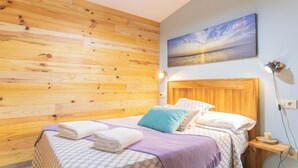 A bedroom with a wooden headboard, a bed with a patterned bedspread, pillows, and a bedside table with a lamp. - 5routes apartments connecting with nature (Vimianzo)