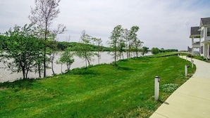 A grassy waterfront area with a sidewalk and trees. - Captain`s Quarters - 179 Leeward Way, Cottage #6 (Ottawa)
