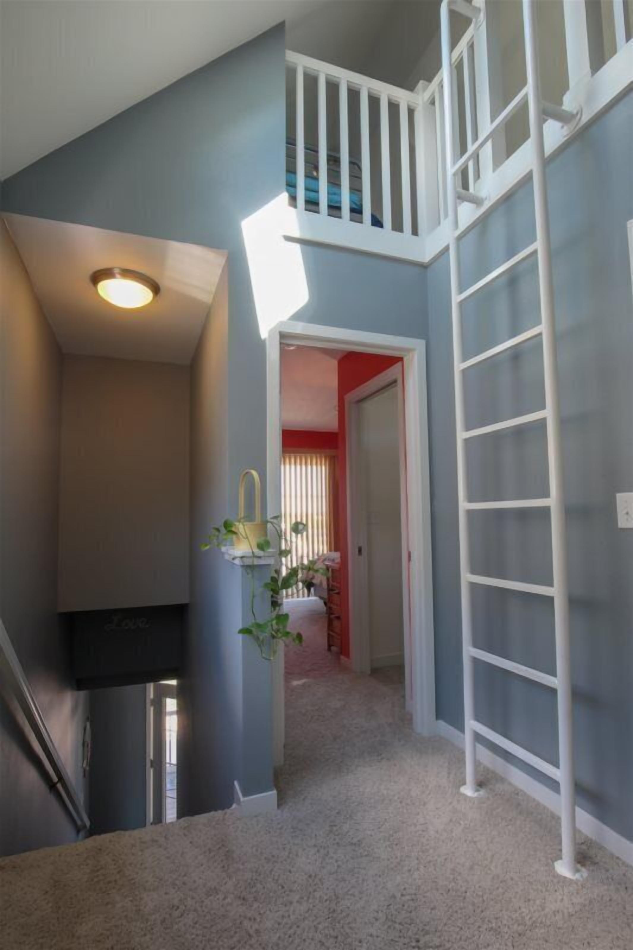 A staircase with a white railing leading to a balcony, a hallway with a beige carpet, and a door leading to a room with red walls.