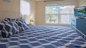 A bedroom with a bed, a TV on a dresser, and a window with a view of trees and houses.