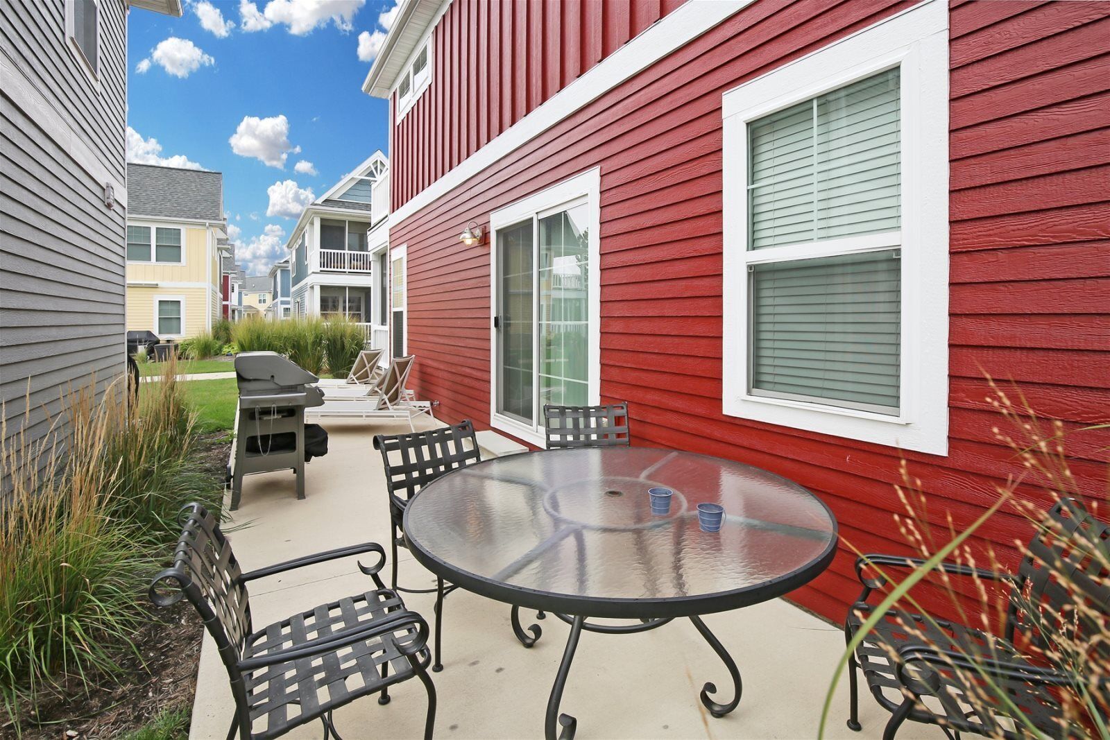 A patio with a round glass table and metal chairs, a sliding glass door, and a red exterior wall.