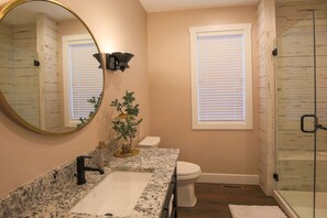 A bathroom with a granite countertop sink, a white toilet, a glass shower enclosure, and a large mirror. - Harbor Master Villa #230 (Ottawa)