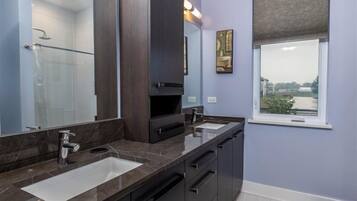 A bathroom with two sinks, dark cabinetry, a large mirror, and a window with a view.