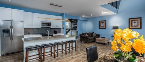 A modern kitchen with a central island, bar stools, and a dining table with chairs.