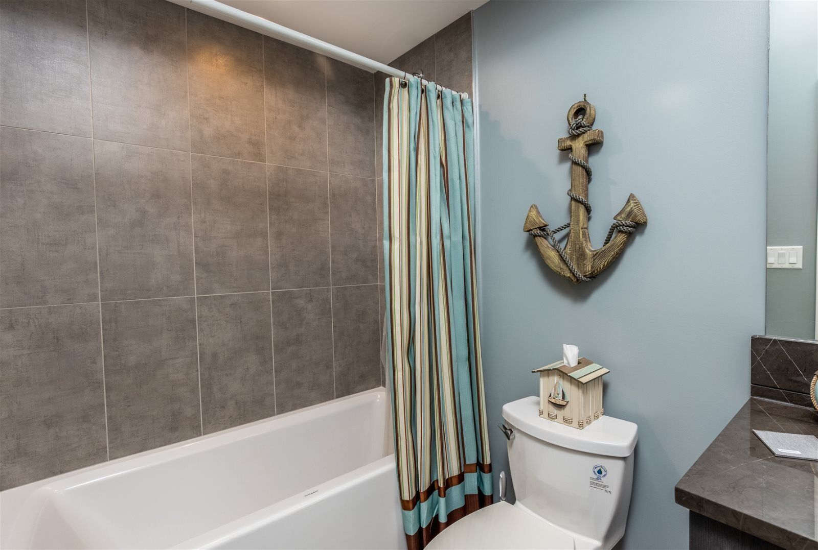 Un baño con bañera, cortina de ducha a rayas, inodoro y un ancla decorativa en la pared.