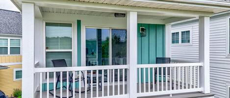 A covered porch with a white railing, a teal door, and a window with a view of trees.