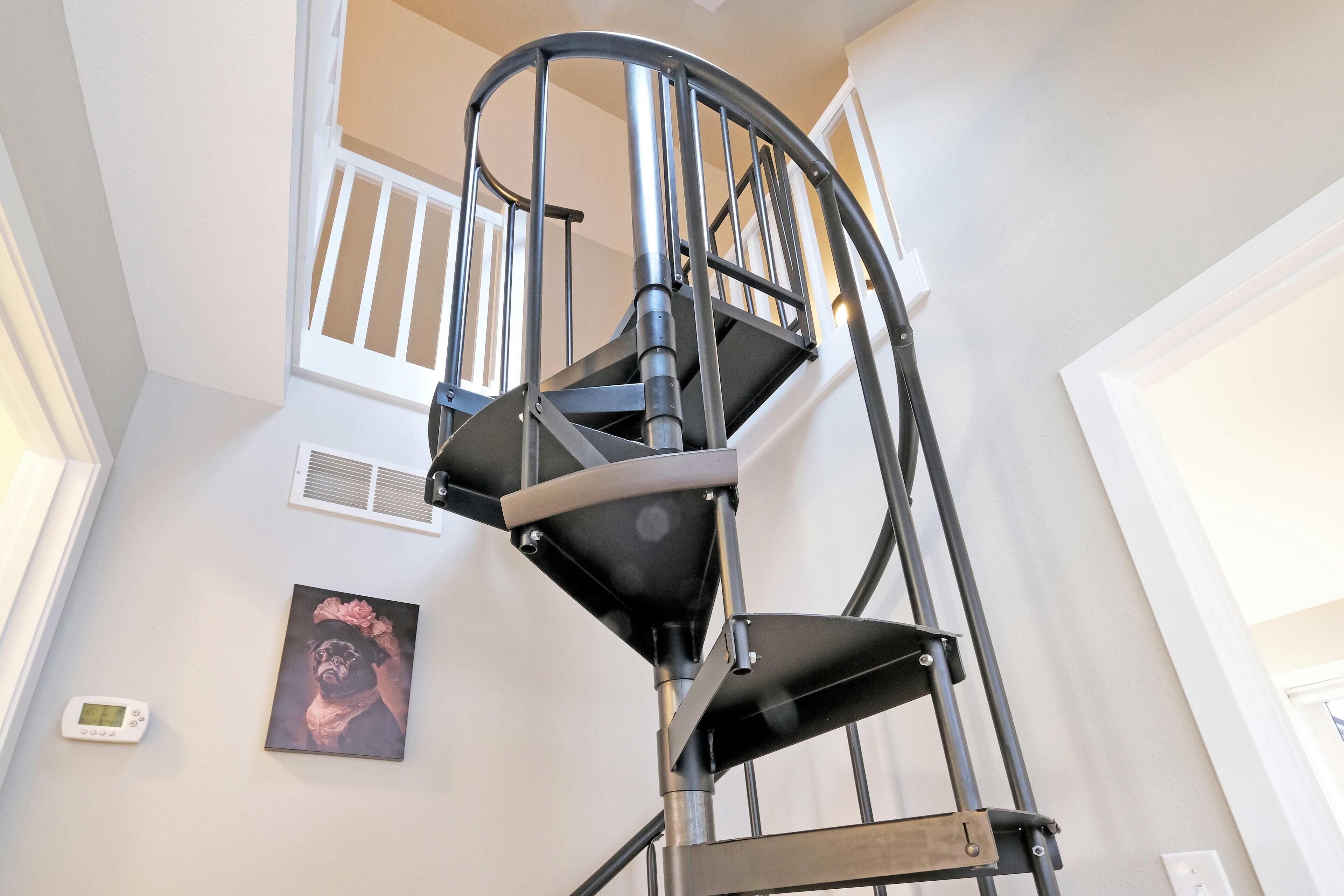 Una escalera en espiral con barandilla de metal, un termostato fijado a la pared y un cuadro enmarcado.