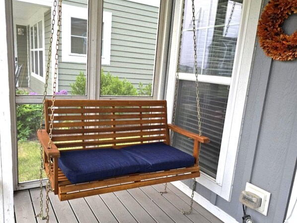 A wooden swing bench with a blue cushion on a porch.