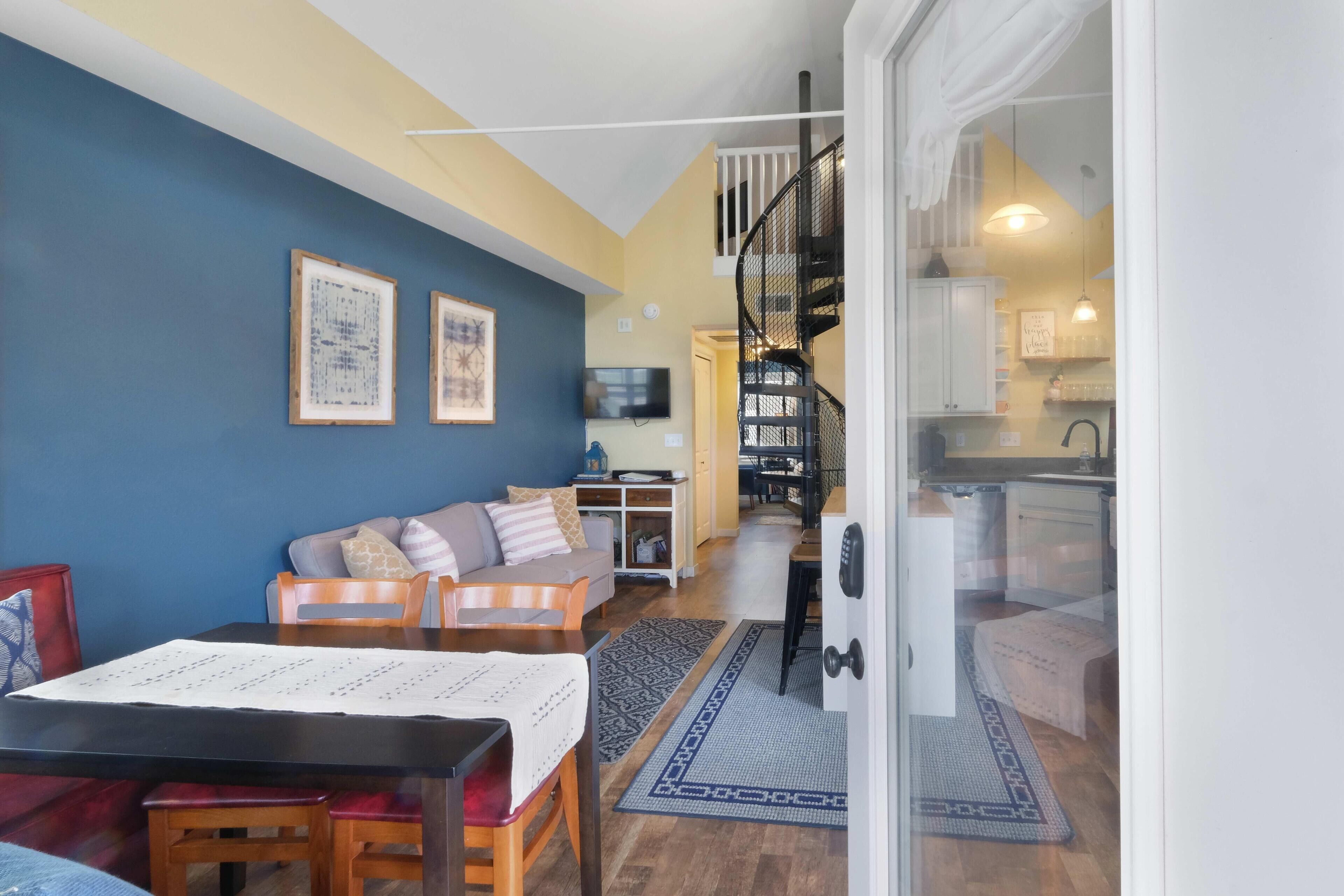 Una sala de estar acogedora con un sofá, una mesa de comedor y una escalera que conduce a una cocina.
