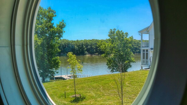 A view through a window of a river, trees, and a house with a balcony. - Our Happy Place #2 (Ottawa)