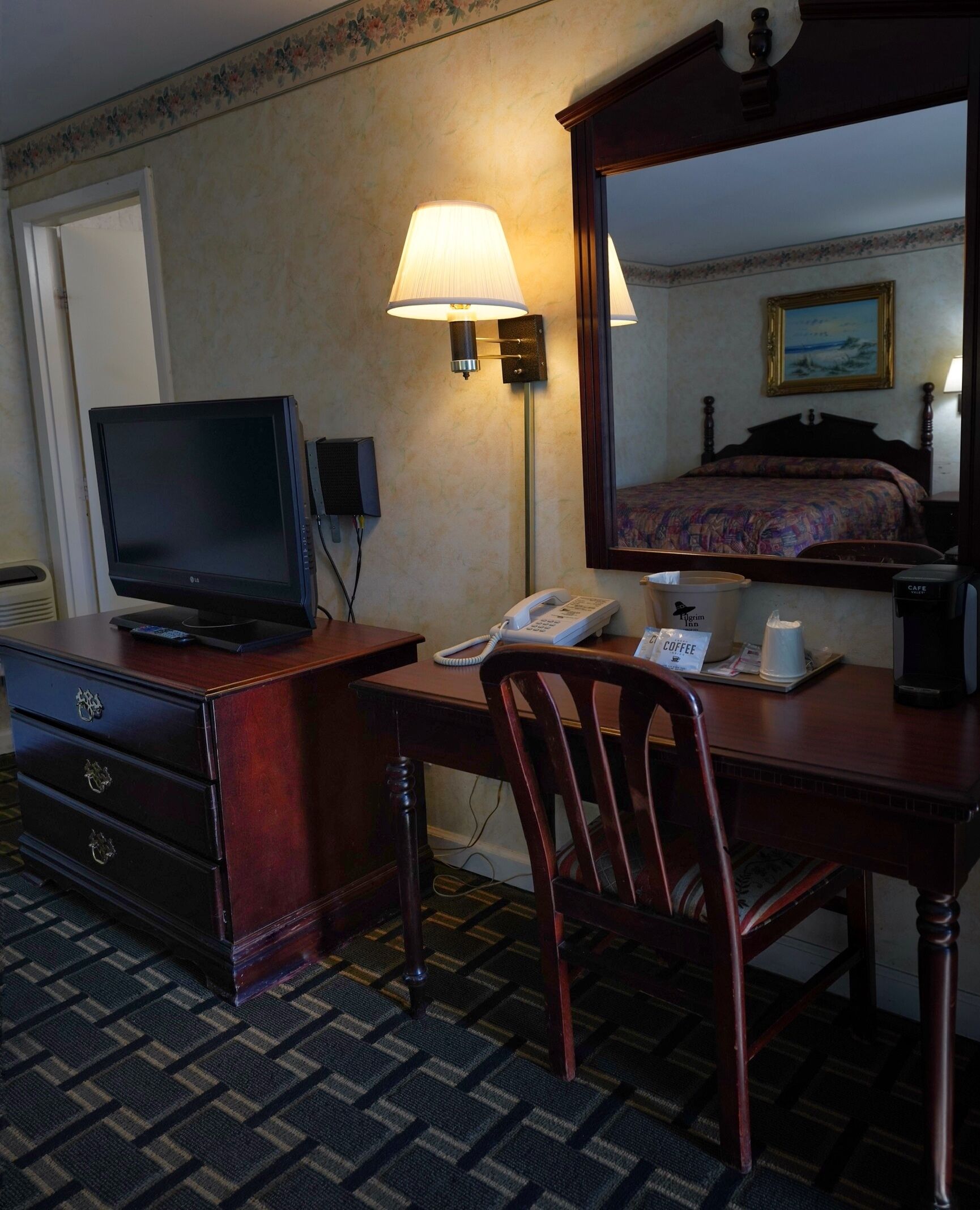 Ein Hotelzimmer mit Schreibtisch, Fernseher, Telefon, Kaffeemaschine und Spiegel.