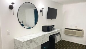 Un baño moderno con tocador de mármol, un espejo redondo, televisor de pantalla plana, microondas y equipo de aire acondicionado.