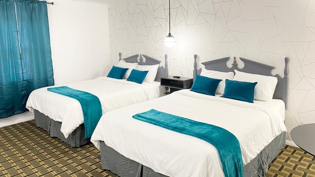 Habitación de hotel con dos camas, una mesita de noche, una lámpara y un suelo con estampado.