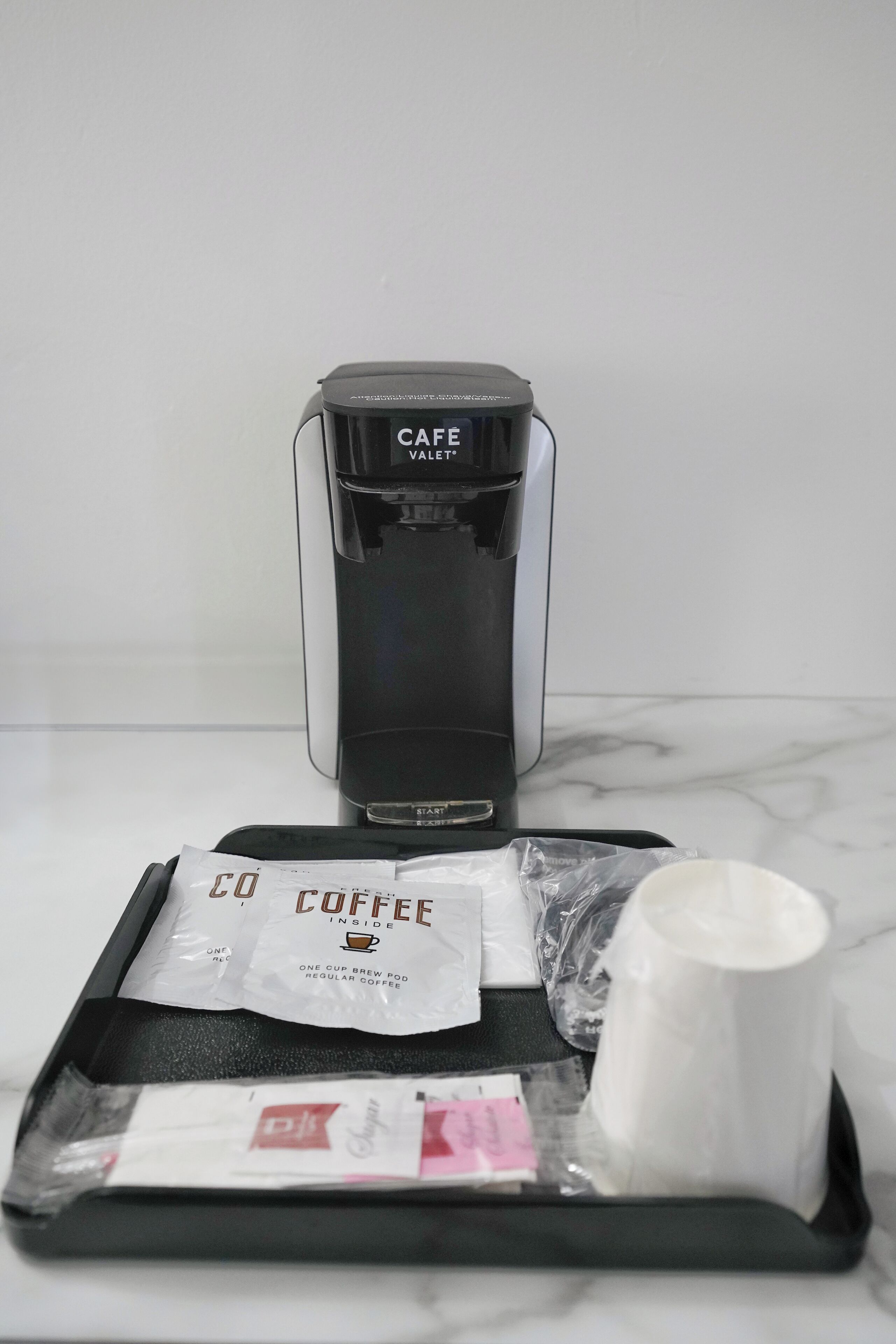 A coffee maker labeled "CAFE" on a tray with a coffee pod, a paper filter, and a plastic bag.