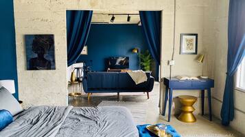 A room with a bed, a desk, a TV, and a plant.